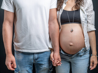 Close-up detail of a young couple holding hands, with the woman who is pregnant and has a bare belly