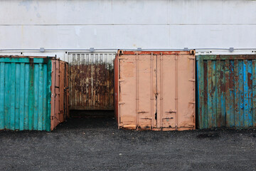 Row Of Old Weathered Shipping Containers In Various Colors With Rust Against White Wall. Industrial Grunge.