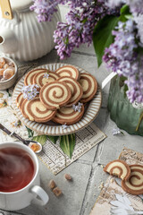 Two colored pinwheal homemade cookies with vanilla and chocolate flavor in shape of spiral on gray tile background with tea and flowers. Cozy breakfast