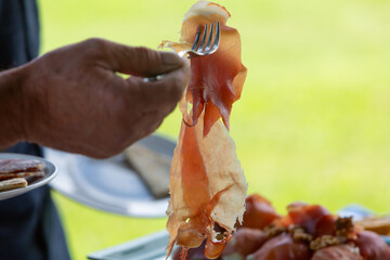 Chef picking up slice of prosciutto with fork at buffet table