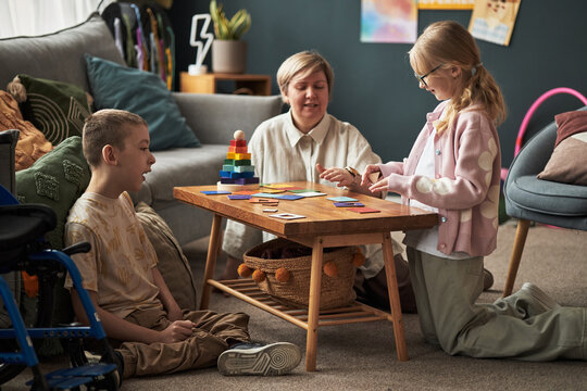 Two children playing educational game with an adult at home, demonstrating focus and cooperation. Cheerful environment with toys and bright decor