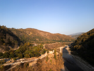 Aerial view of a mountain river winding through rocky terrain, illuminated by warm sunrise or sunset light. Majestic landscape captured from above with serene natural beauty.