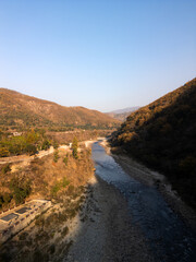 Drone shot of a crystal-clear mountain stream cutting through rugged hills under the golden glow of morning light. A peaceful, untouched wilderness full of harmony and warmth.