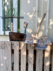 Assorted garden tools including rakes, hoes, and shovels on a rustic pallet under natural light, with space for text.