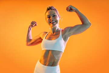 Strong mature woman showing muscles and smiling on orange background