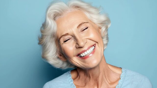 Joyful elderly woman with beautiful smile and bright eyes against a blue background, representing happiness and positivity in aging and life experiences