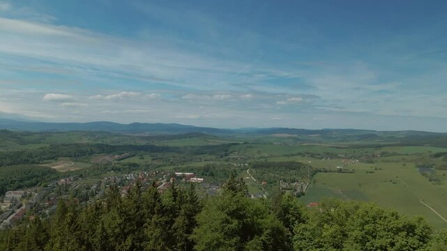 Drone view looking over tree-covered hills and wide green fields stretching across the Bogusz&oacute;w-Gorce landscape toward distant mountain ranges