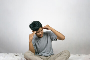 Portrait Of Depressed Young Indonesian Man Sitting On Bed At Home, Suffering Life Problems Or...