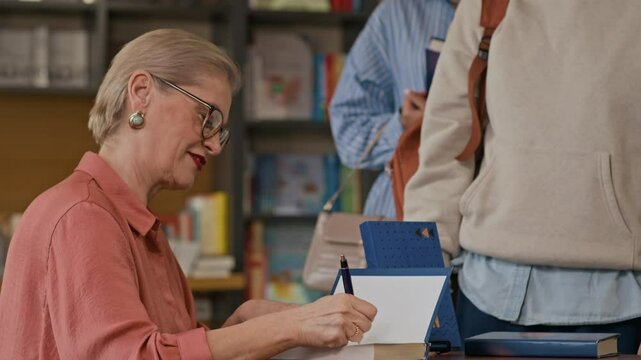 Group of excited diverse readers lining up in bookstore to meet author and get their books signed during warm literary gathering in cozy setting