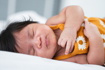 Mixed race, Asian and African, newborn one month baby girl sleeping on bed lying on white sheets....
