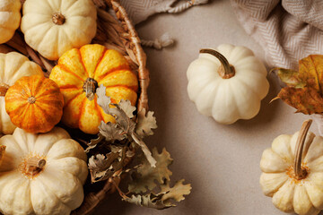 Flat lay composition of white and orange pumpkins with dried oak leaves and cozy blanket