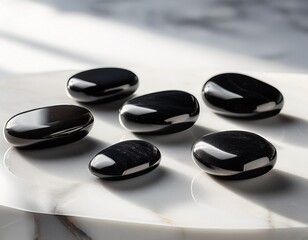five polished black obsidian stones rest on a white marble slab bathed in soft light