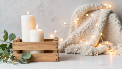 Two white candles in wooden crate with cozy blanket and fairy lights  