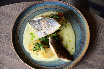 Background View of Sea Bream Dish with Hollandaise Sauce, Potatoes, and Fresh Herbs in Restaurant