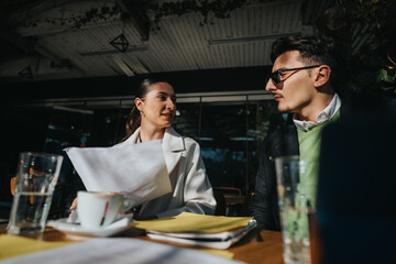 A young pair of colleagues engage in an outdoor business meeting, reviewing documents and discussing plans under warm sunlight, fostering an atmosphere of collaboration, professionalism, and teamwork.