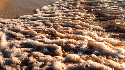 white sea foam dissolving on the sand on a summer afternoon. Golden sunlight illuminates the foam
