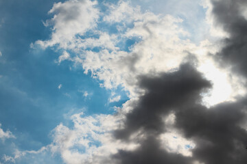 The sun hidden behind a mass of dark grey clouds, with rays of light and shadows on blue sky, for background