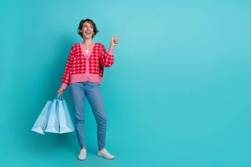 Gordijnen Full length photo of positive impressed lady wear pink cardigan holding shoppers showing emtpy space isolated teal color background © deagreez