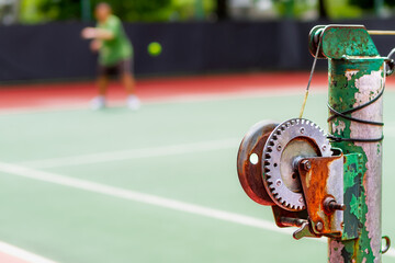Old and rustic tennis net reel post with blurred person taking tennis lesson on the background
