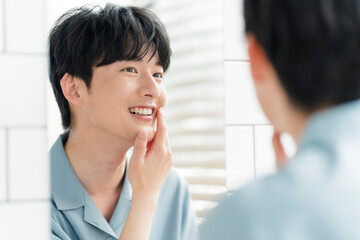 メンズビューティー /スキンケア /鏡を見ながら肌を触っている若い日本人男性。	