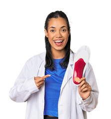 Young Filipina podiatrist with insole smiling and pointing aside, showing something at blank space.