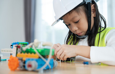 Young Girl Building Robot: A focused young girl, wearing a white hard hat, meticulously assembles a...