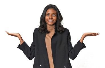 Young Indian woman in business suit makes scale with arms, feels happy and confident.