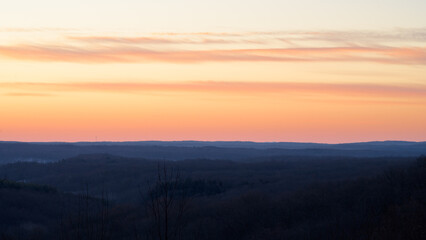 Fototapeta premium Vibrant colors fill the sky as the sun sets over distant hills, creating a peaceful atmosphere in the quiet landscape. This serene moment captures the beauty of nature.