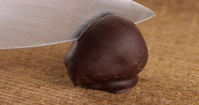 Freeze-dried strawberries in dark chocolate are cut with a knife on a wooden board background.