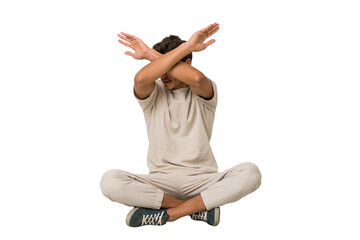 Young caucasian man sitting on the floor isolated on white background keeping two arms crossed,...