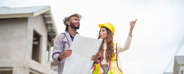Male and female construction workers wearing hard hats and safety vests discussing building plans on site, man holding blueprint, teamwork and project planning