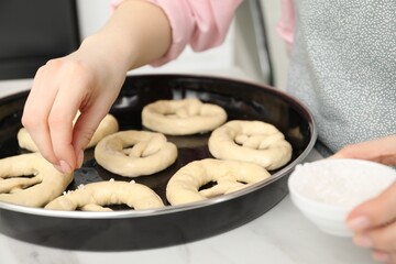 Woman adding sea salt onto uncooked pretzels at table indoors, closeup