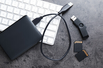 SD memory cards, USB flash drive, hard disk drive with cable and keyboard on dark grey table, flat...
