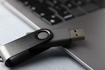 Flash drive and laptop on light grey table, closeup