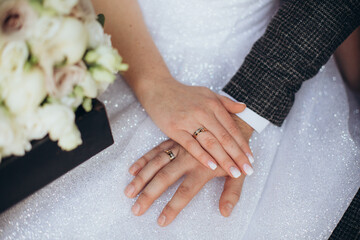 Bride and groom hands with wedding rings on white sparkling dress background. Woman's manicured...