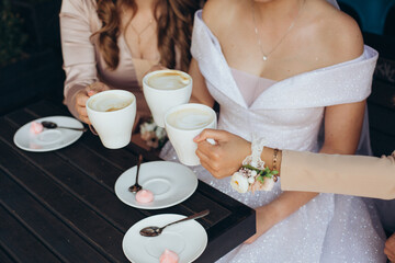 Three women in elegant dresses holding coffee cups outdoors. Bright dresses, delicate wrist...