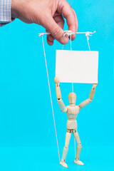 Male hand controlling a wooden mannequin with white thread attached, manipulation concept on blue...