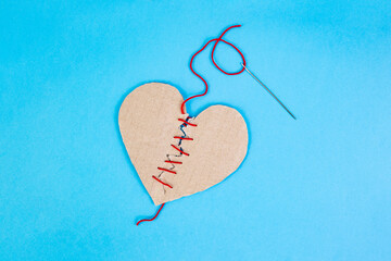 Broken cardboard heart sewed together with a needle and red thread on blue background, marriage counseling concept