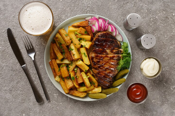 juicy barbecue steak with fried potatoes in a restaurant, served with beer, fresh vegetables and pickles, ketchup and mayonnaise