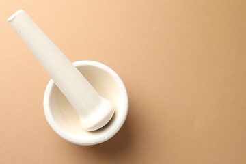 Ceramic mortar and pestle on light brown background, top view. Space for text