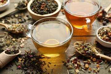 Different herbal teas and dry leaves on wooden table, closeup