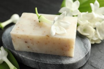 Bar of soap and jasmine flowers on black table, closeup