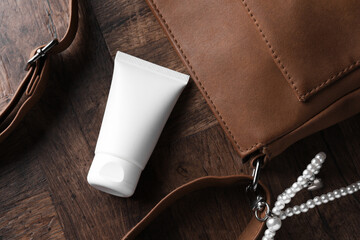Tube of moisturizing body cream and leather bag on wooden table, flat lay