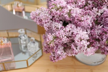 Beautiful lilac flowers in glass vase and perfumes on wooden table indoors, closeup
