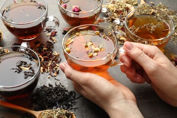 Woman with aromatic herbal tea, dry leaves and flowers at grey table, closeup