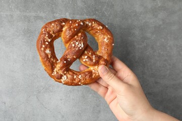 Woman with tasty pretzel near grey textured wall, closeup