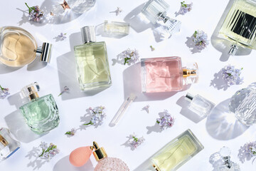 Luxury perfumes and beautiful lilac flowers on white background, flat lay