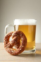 Tasty pretzel and glass of beer on wooden table against grey background, closeup