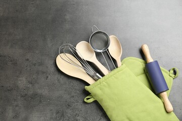 Different kitchen utensils in oven mitten on grey table, flat lay. Space for text