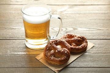Tasty pretzels and glass mug of beer on wooden table, closeup